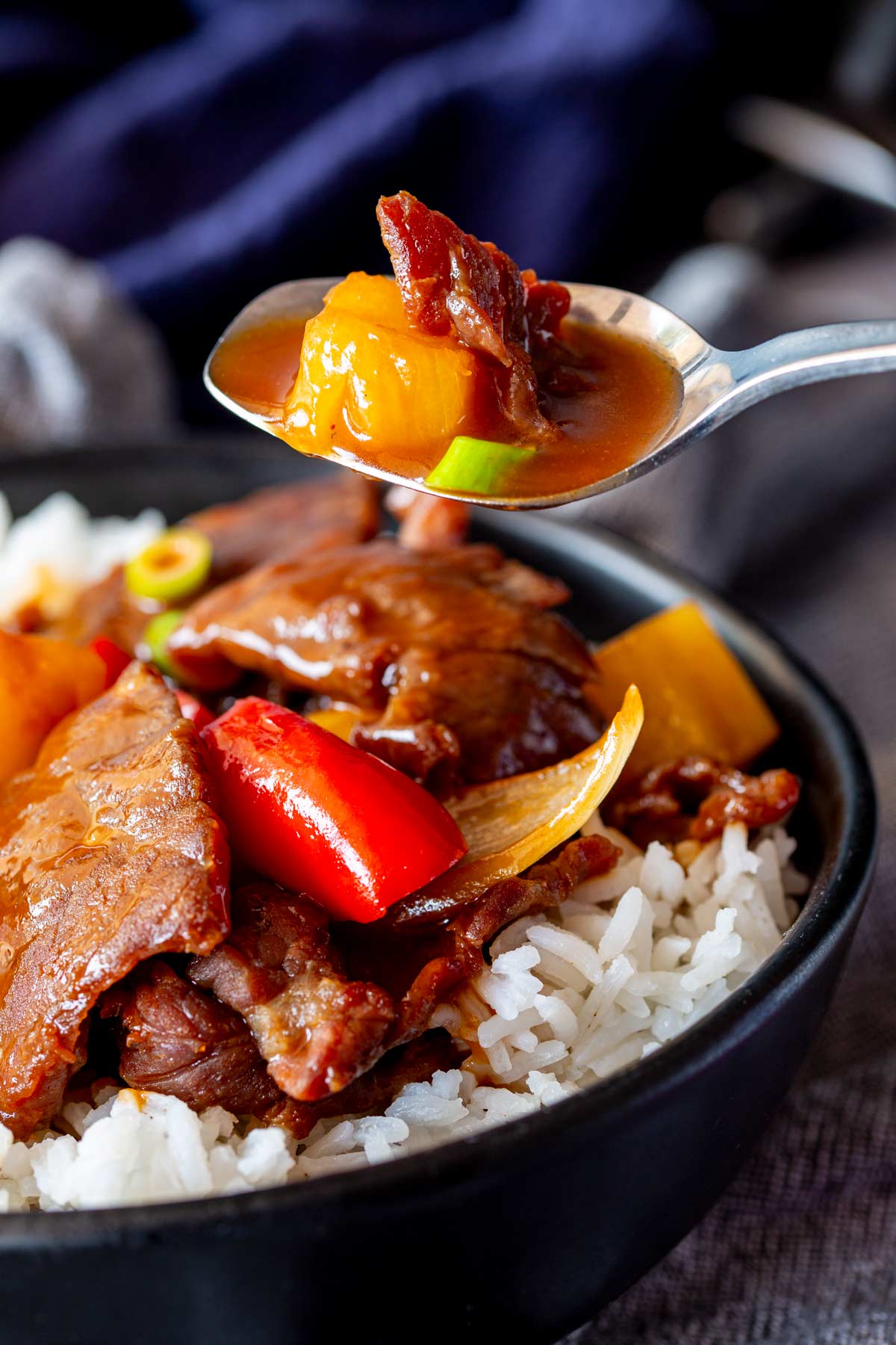 Close-up of sweet and sour beef being lifted with a spoon, showing sauce and vegetables