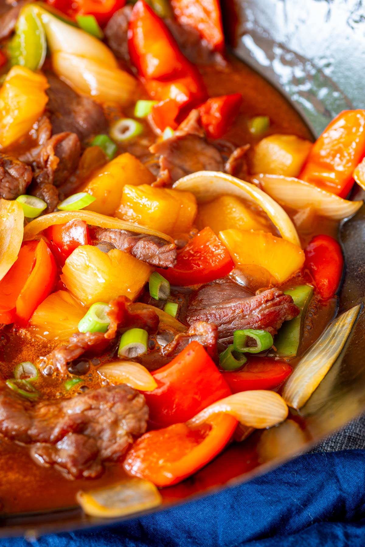 Stir-fried beef in a wok with colorful bell peppers, onion and pineapple with a red sauce