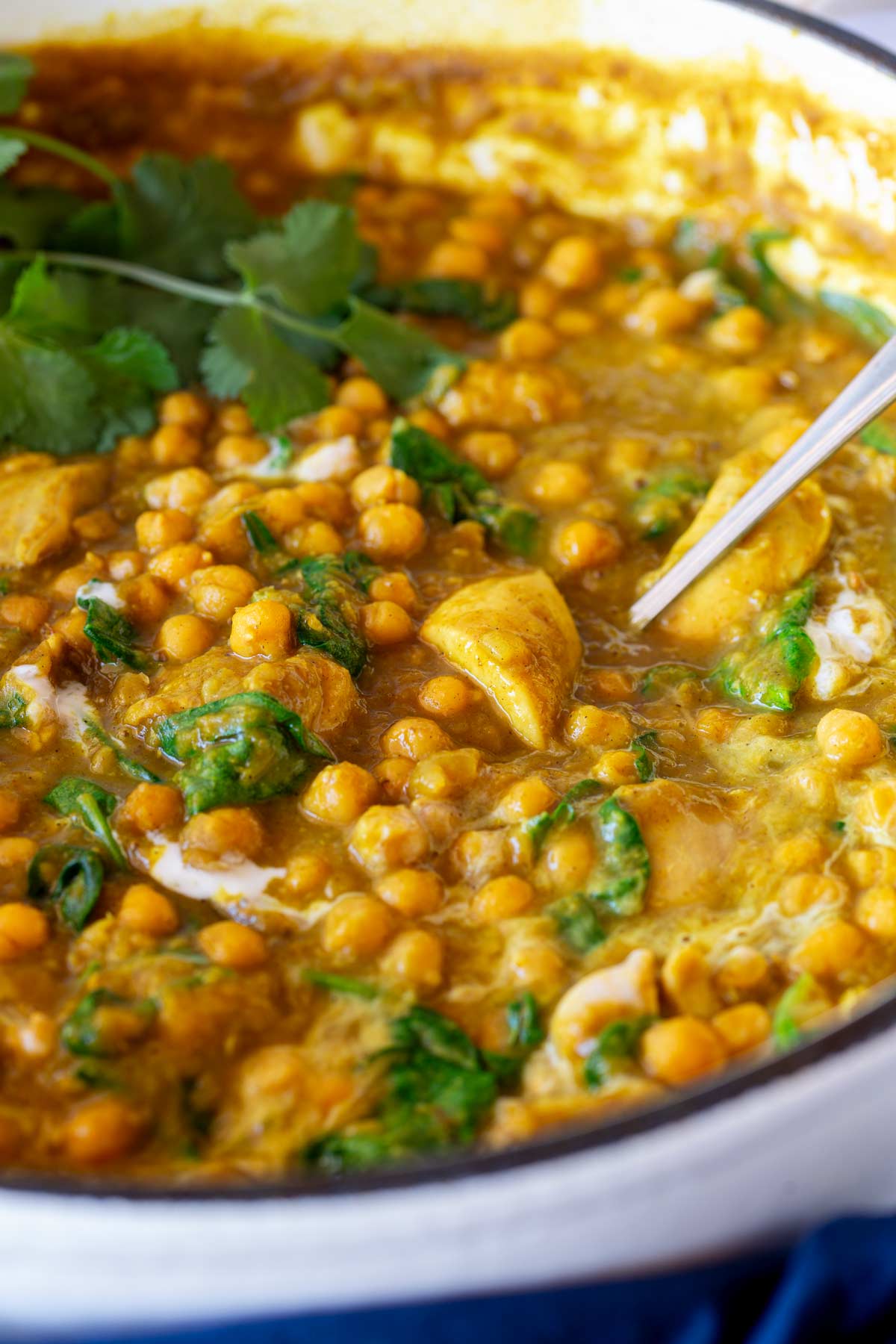 Curry with chickpeas, chicken, and greens in a round light-colored pan, with a spoon