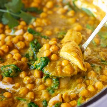chicken and chickpea curry being scooped out of a pan with a silver ladle