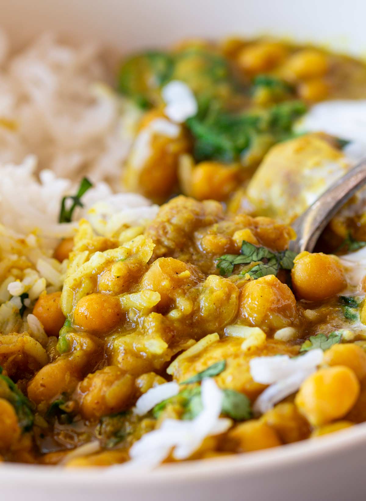 Curry with chicken, chickpeas, and spinach in a cream bowl with rice and a spoon resting inside