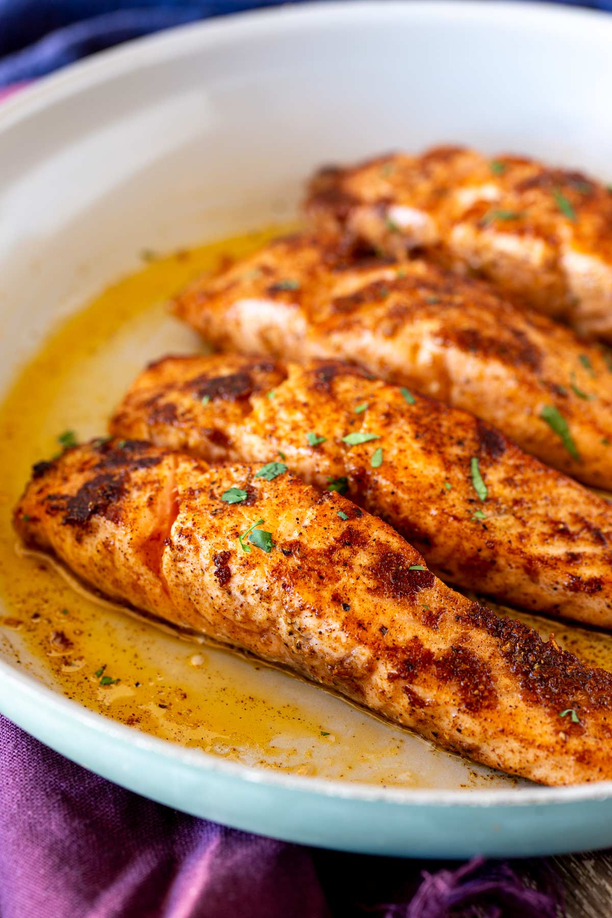 Four salmon fillets cooking in a light coloured skillet, lightly browned and sprinkled with chopped cilantro