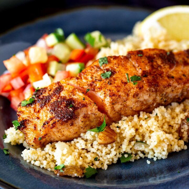 close up of a salmon fillet with lemon nut couscous, tomato salad, chopped herbs and a wedge of lemon