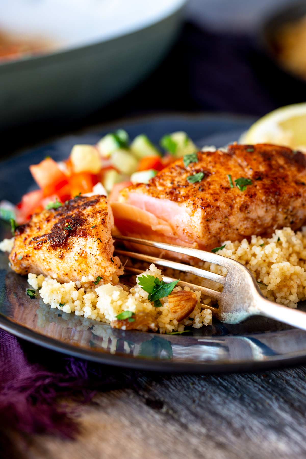 Close-up of a fork pulling apart a salmon fillet, showing its golden crust and juicy, flaky texture.