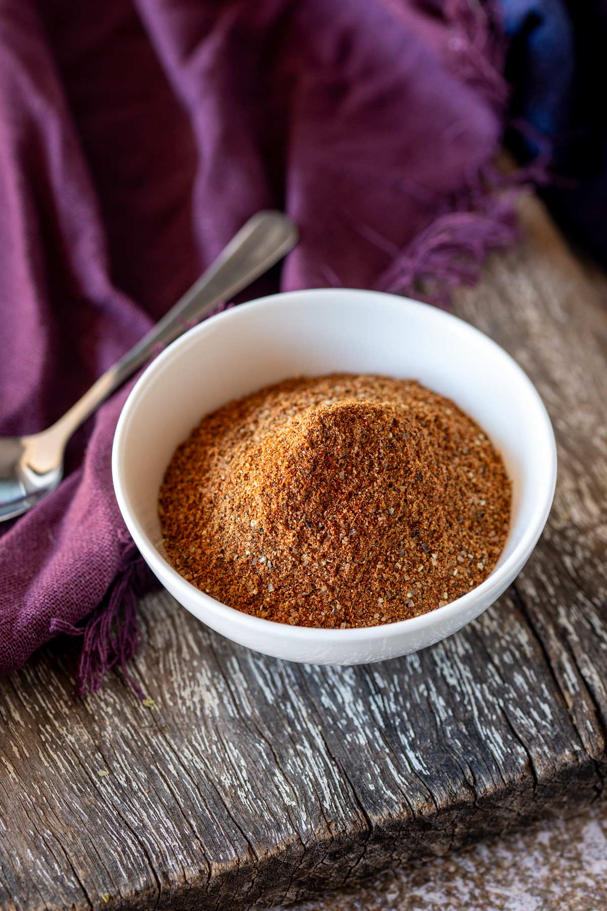 a wooden board with a bowl of spices on it and a spoon and purple napkin