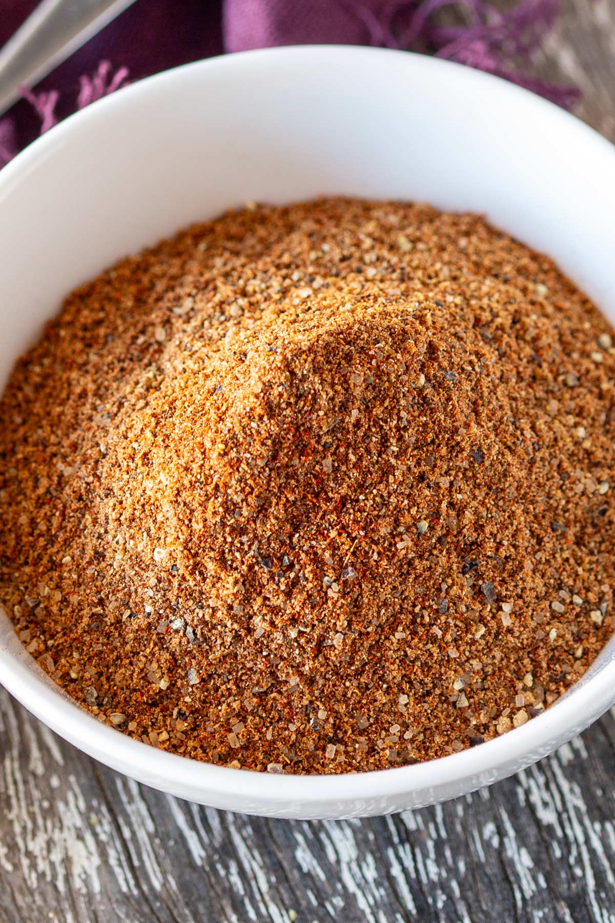 Overhead view of a rustic wooden board with a white bowl of a spice blend