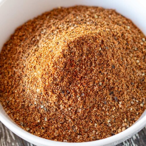 Overhead view of a rustic wooden board with a white bowl of brown spices