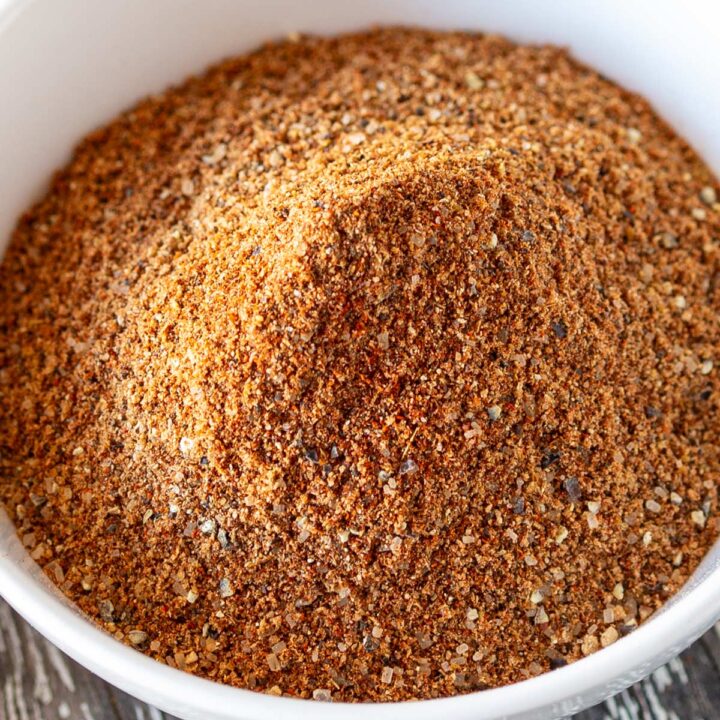 Overhead view of a rustic wooden board with a white bowl of brown spices