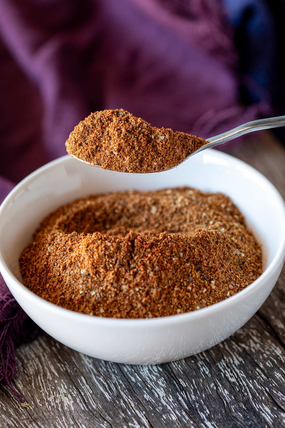 a silver spoon scooping up some moroccan seasoning from a white bowl