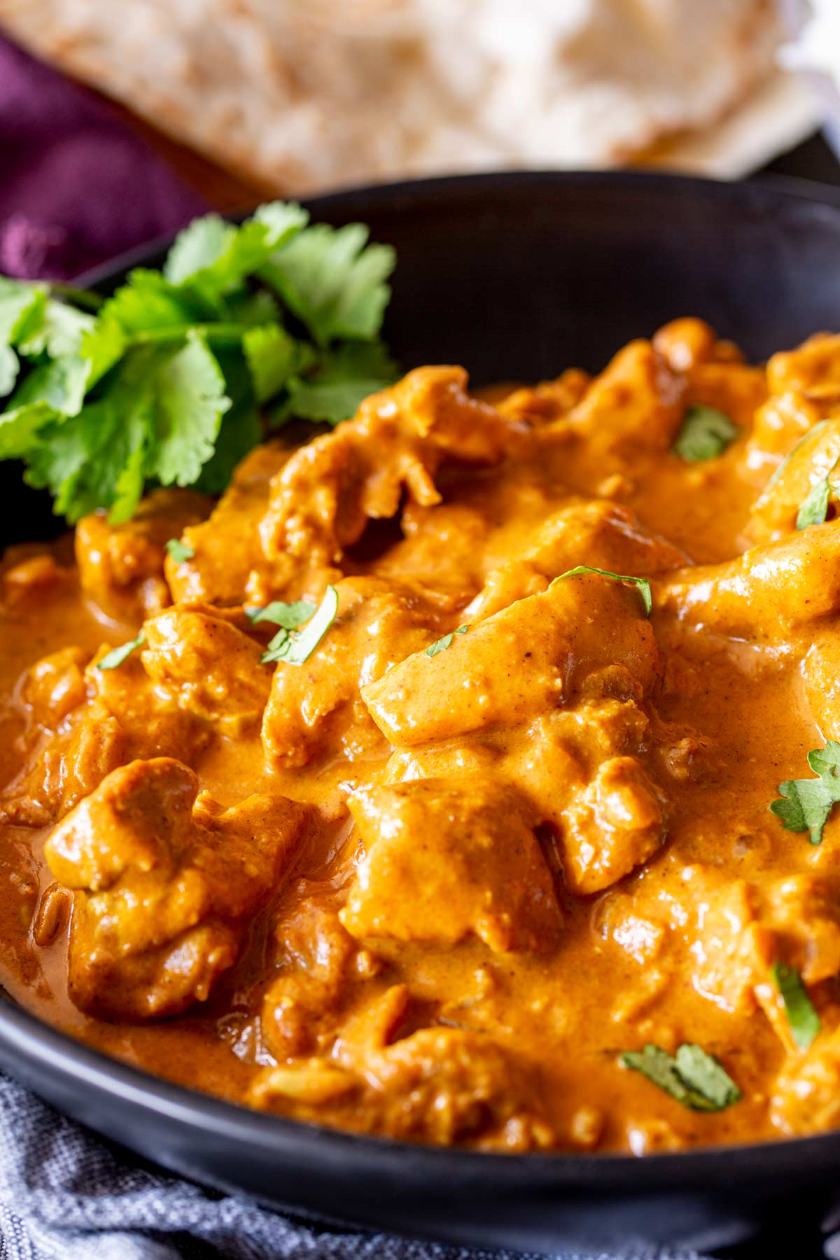 A dark bowl filled with golden Chicken Korma, garnished with cilantro