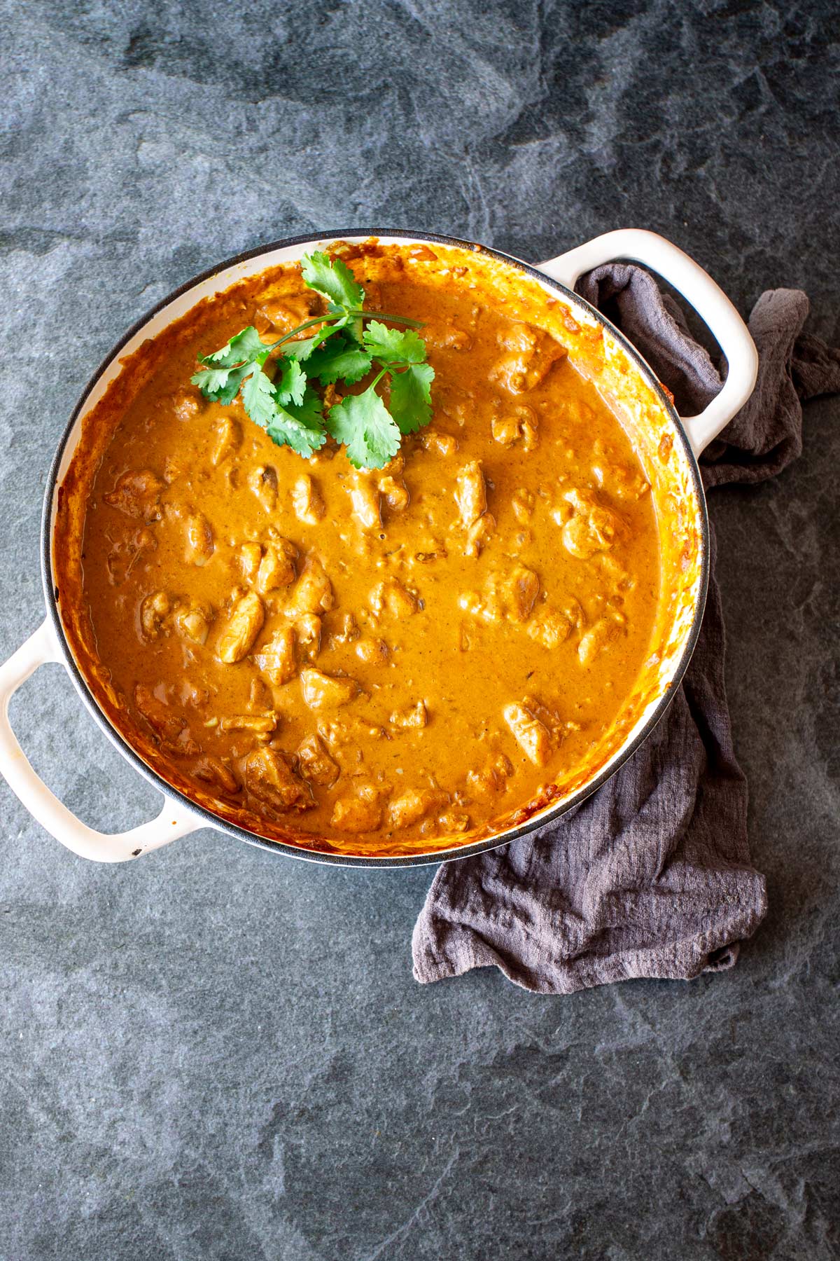 Chicken Korma in a cream cast iron pan on a dark bench with grey linen