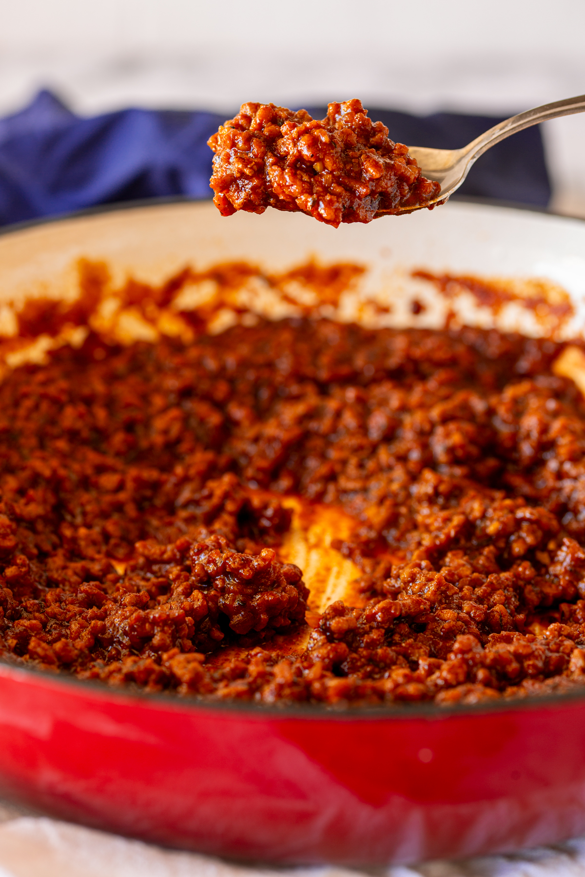 A spoonful of homemade chili sauce for hot dogs, held above the skillet