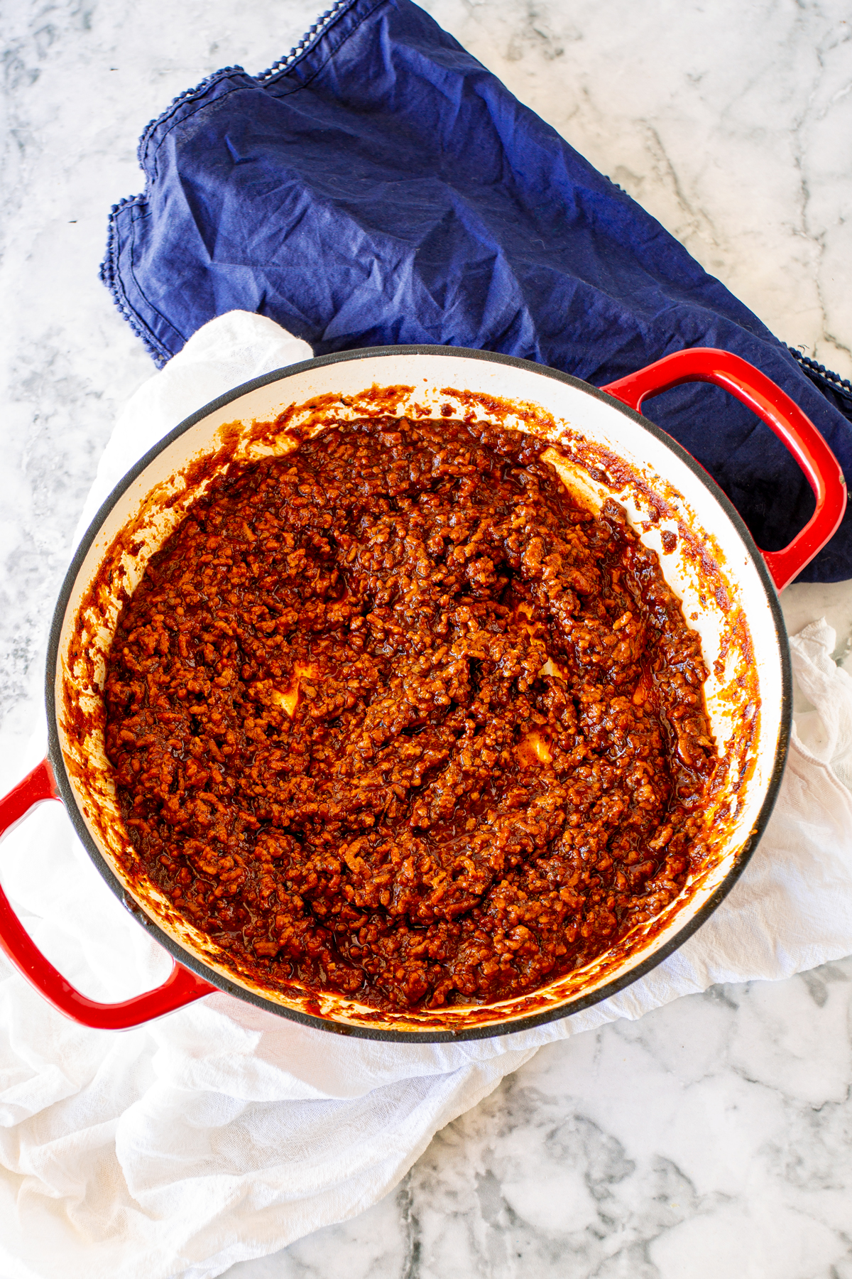 Red skillet filled with beef chili sauce, photographed from overhead on marble counter