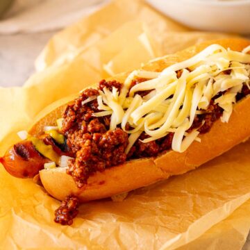 A cooked hot dog in a bun topped with chili sauce and cheese, ready to serve