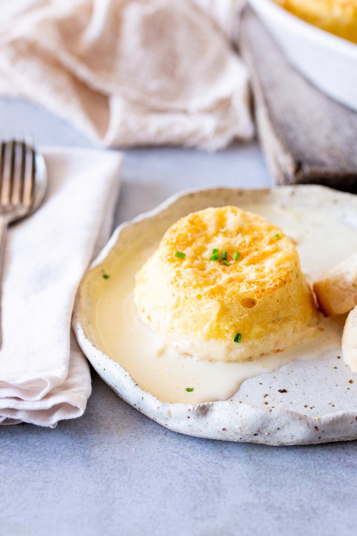 Single cheese soufflé on a rustic plate with cream linen and a vintage fork
