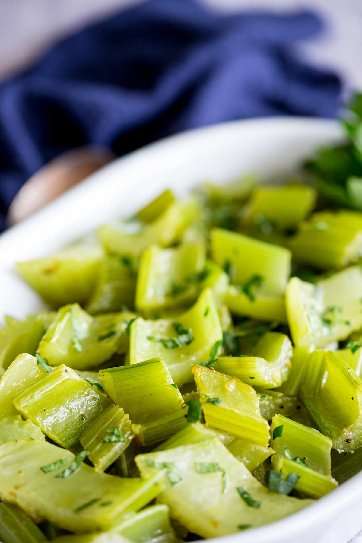 a white dish with braised celery in it with a rustic spoon and blue napkin in the background