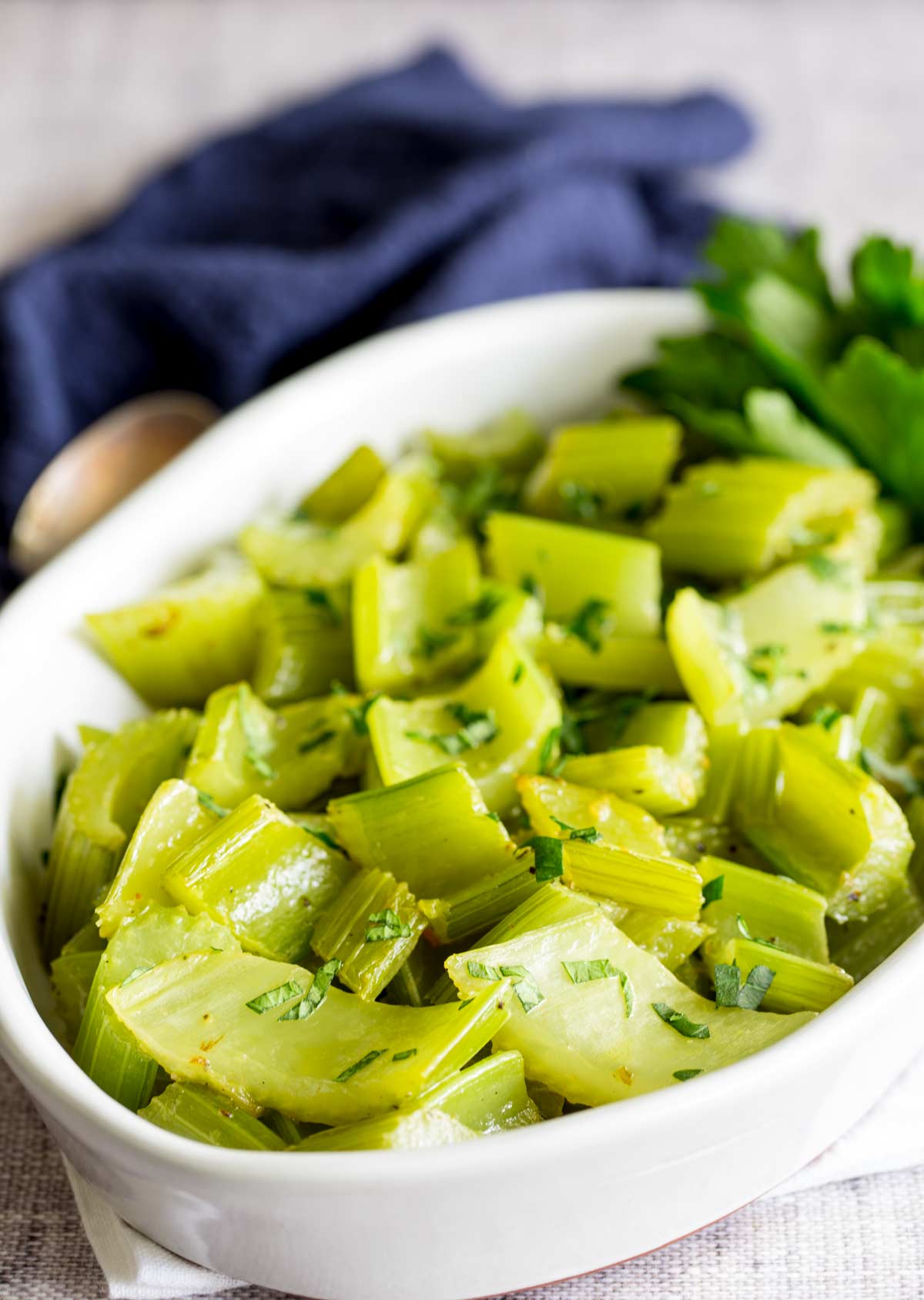 a light coloured table with a white bowl of chopped and cooked celery in it with a. blue napkin behind