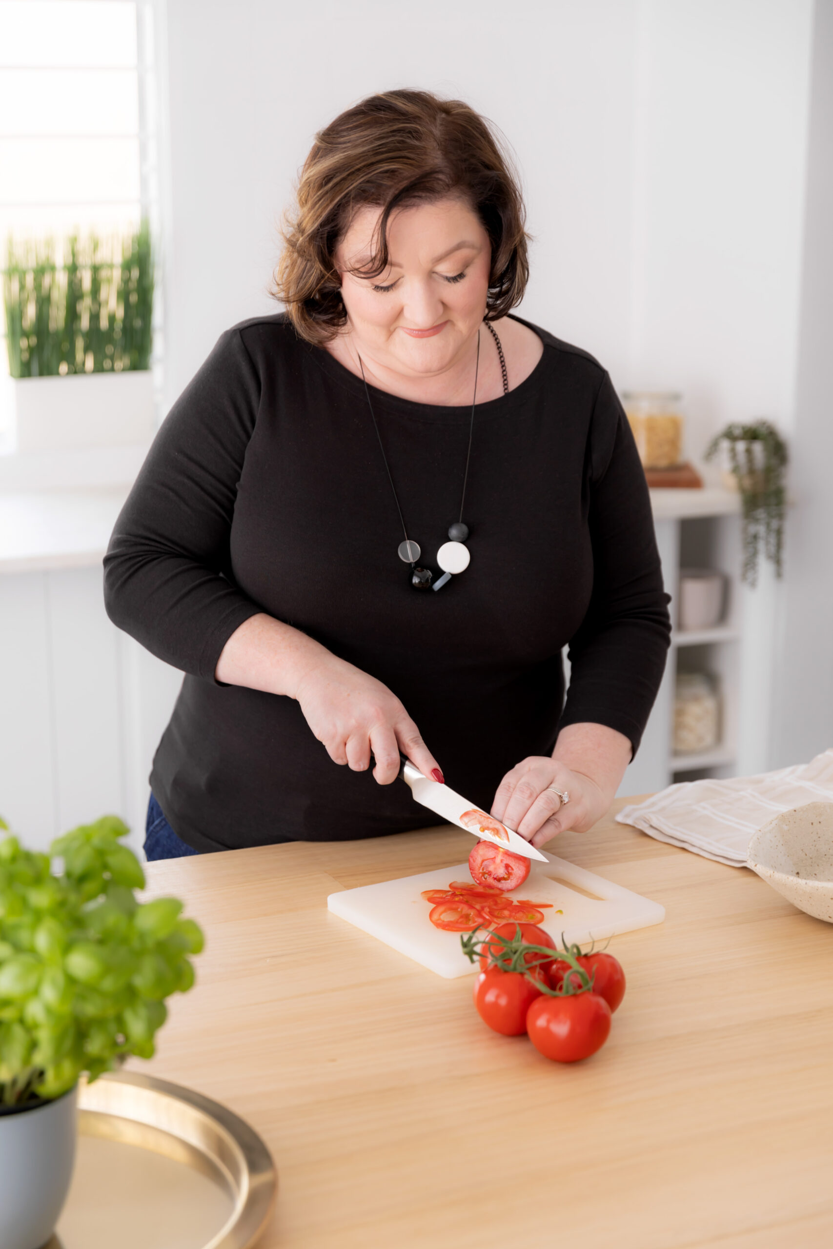 a lady in a black top cutting tomatoes on a small chopping board
