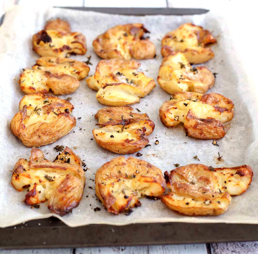 12 squashed roasted potatoes on a lined baking sheet