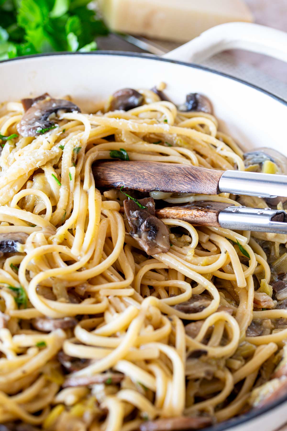 Cream cast iron pan filled with mushroom and leek pasta with tongs ready to serve