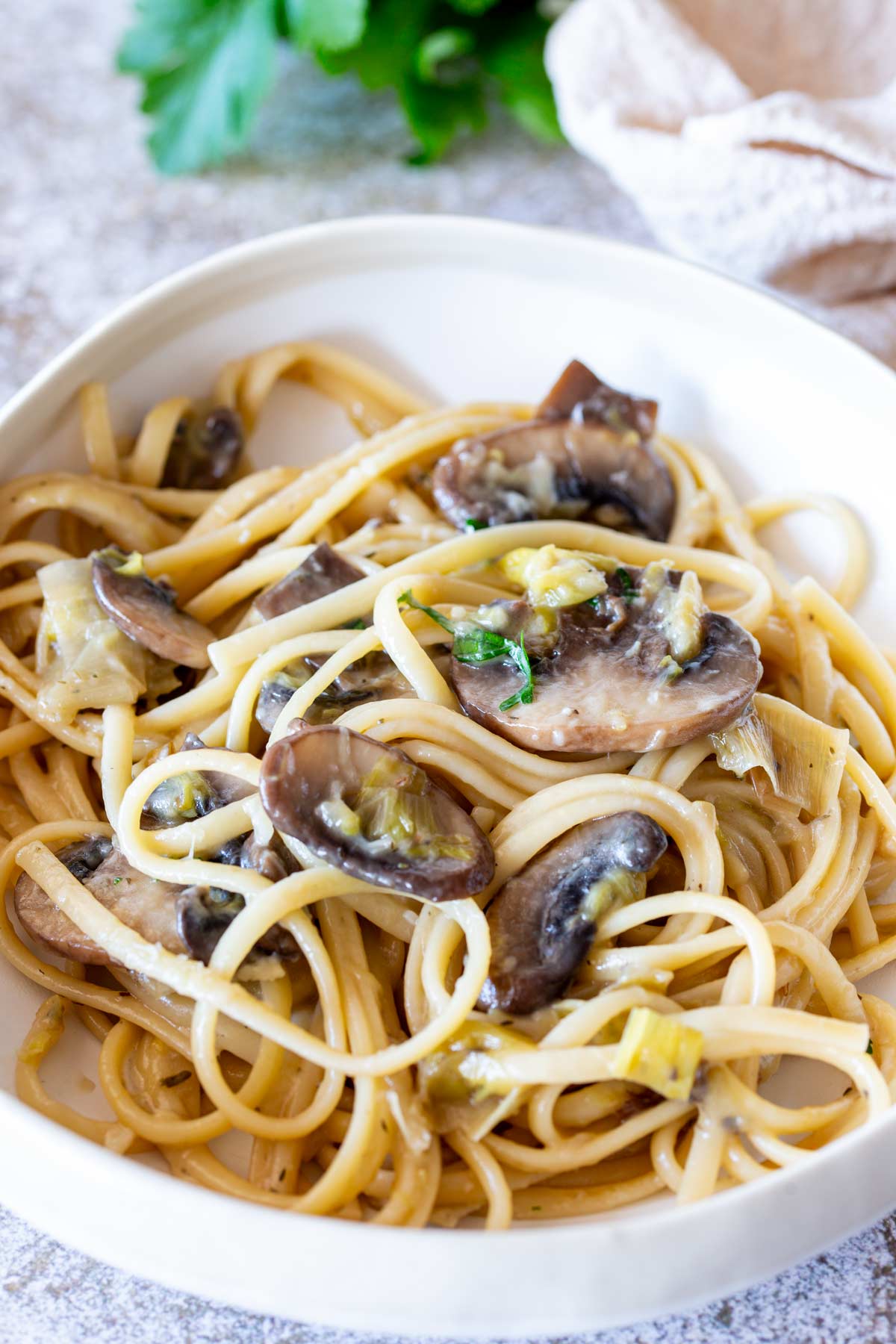 Cream bowl of pasta on a stone table with parsley in the background