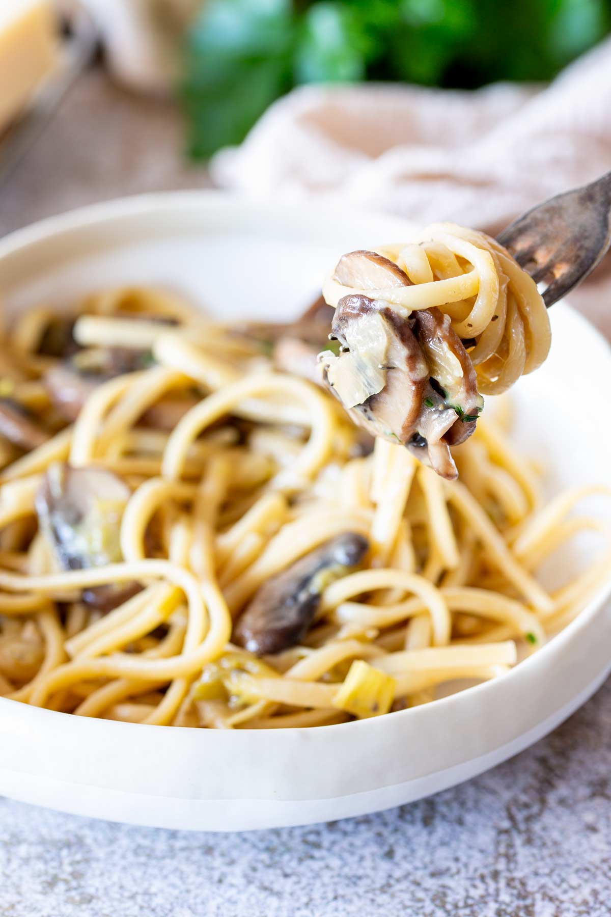 Fork lifting up mushroom and leek linguine from a cream bowl