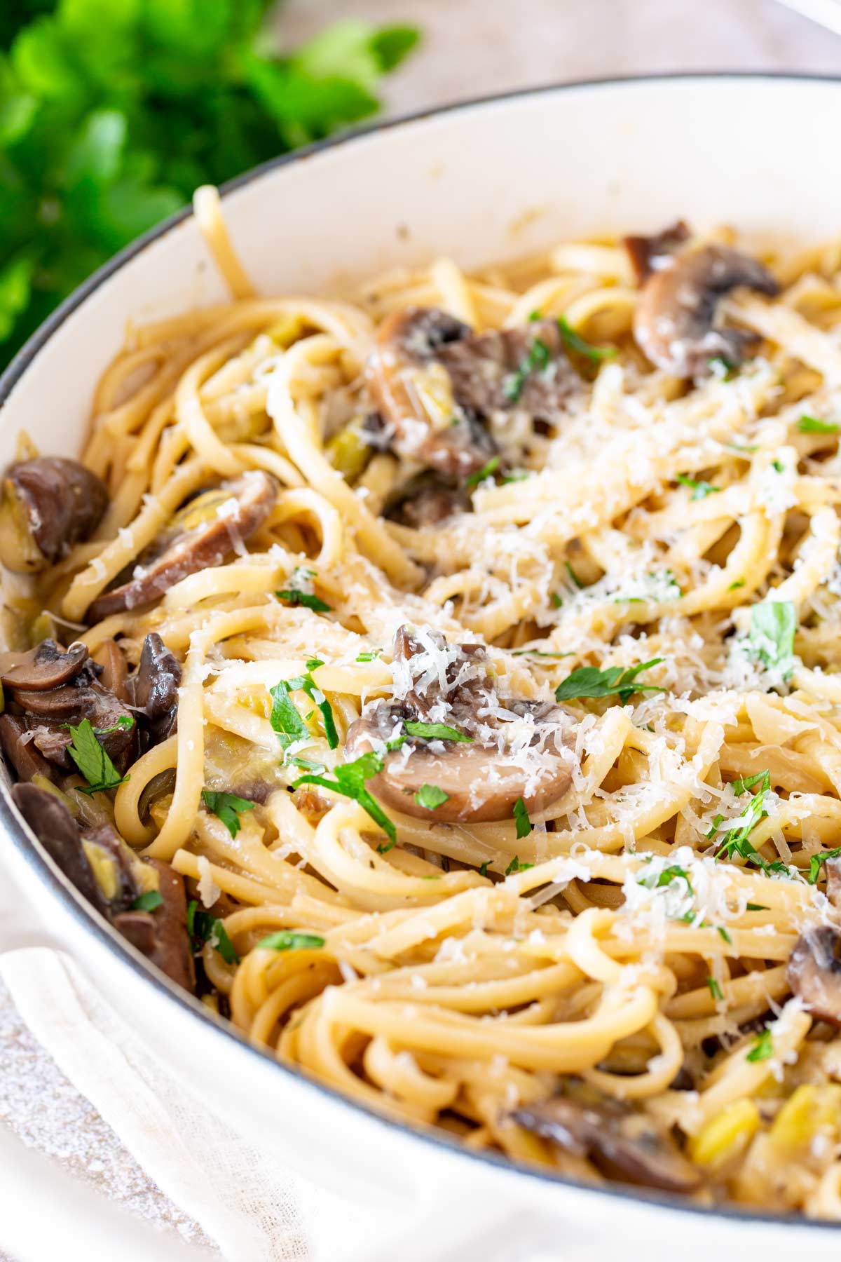 Side angle of a cream cast iron pan filled with pasta and mushrooms with herbs in the background