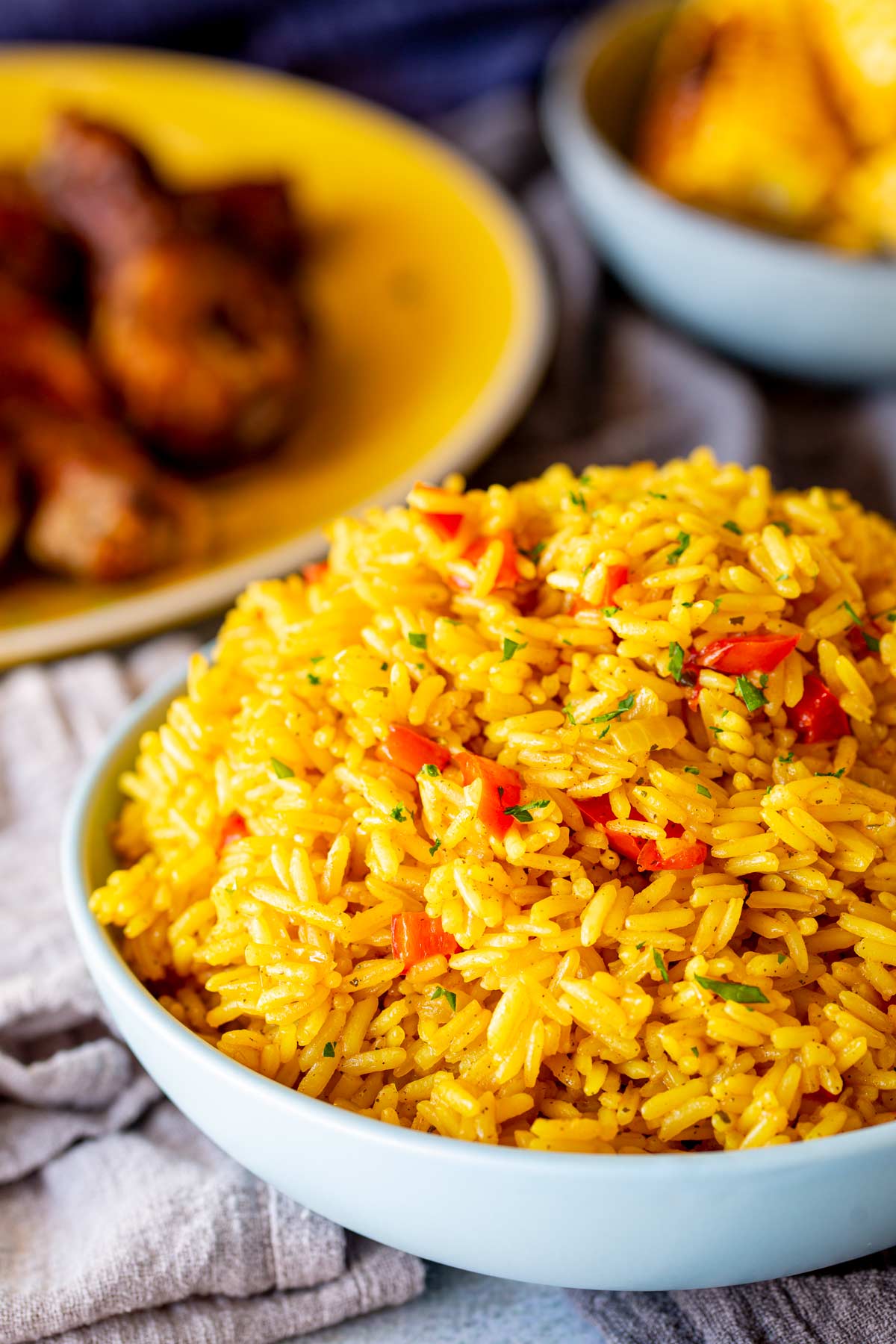 yellow rice in a blue bowl with peri-peri chicken and grilled corn blurred in the background