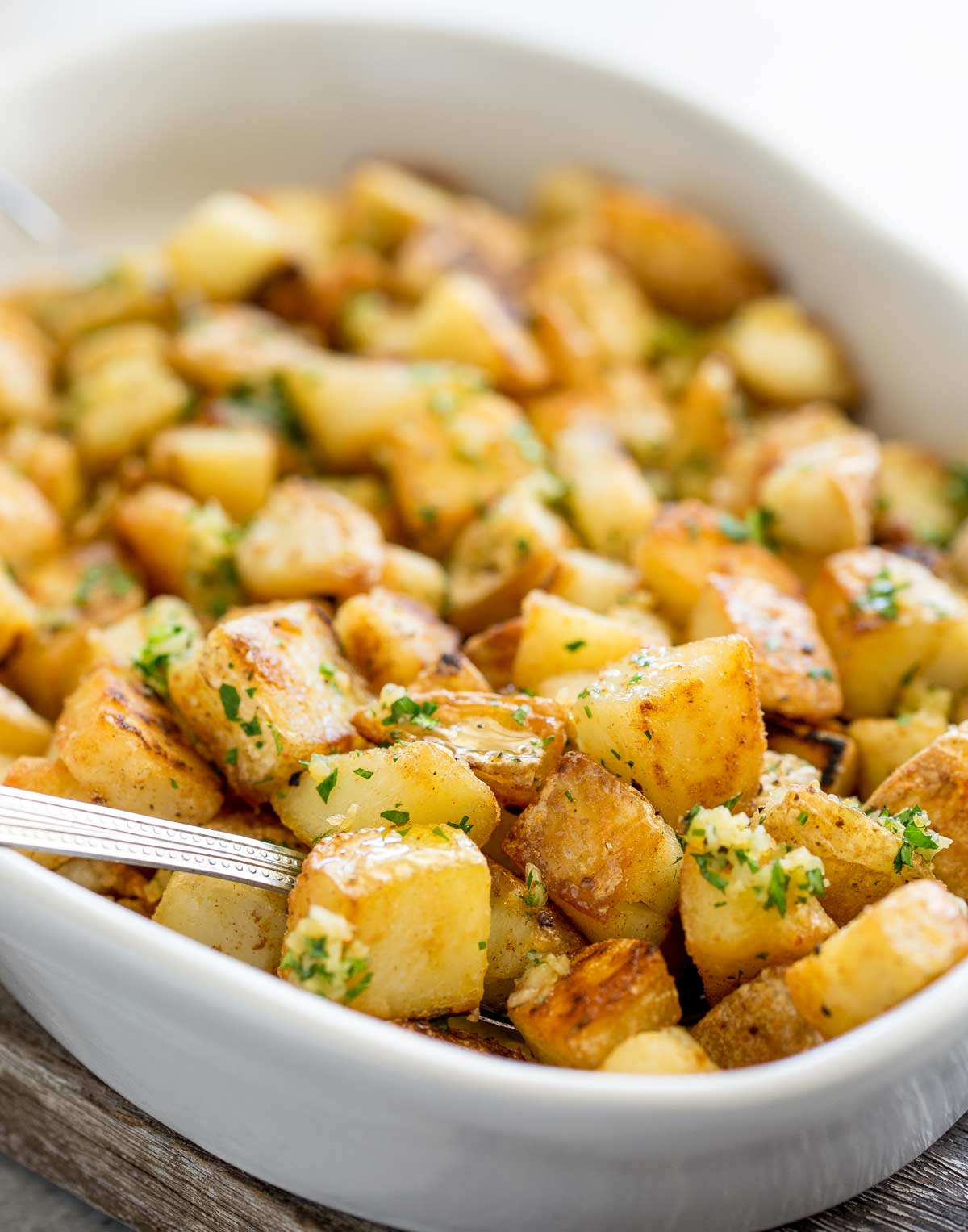a spoon in a dish of crispy potatoes topped with garlic and parsley