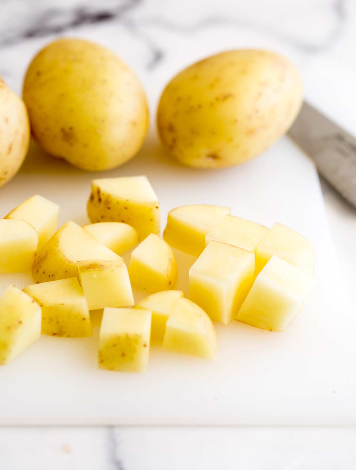 cubed potatoes on a white chopping board with whole potatoes in the background