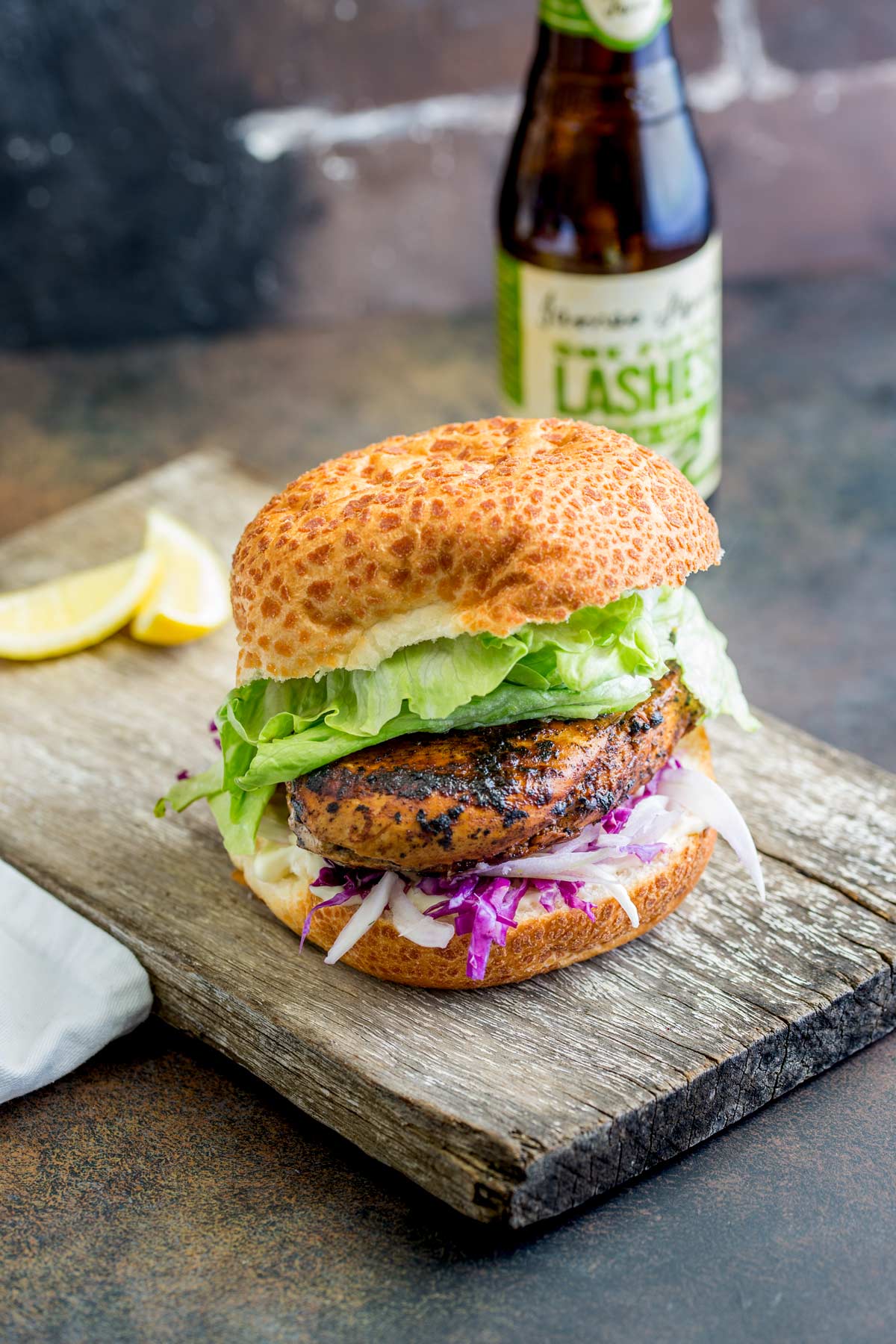 Peri Peri Chicken Burgers with lettuce on a rustic wooden board with lemon wedges in the background