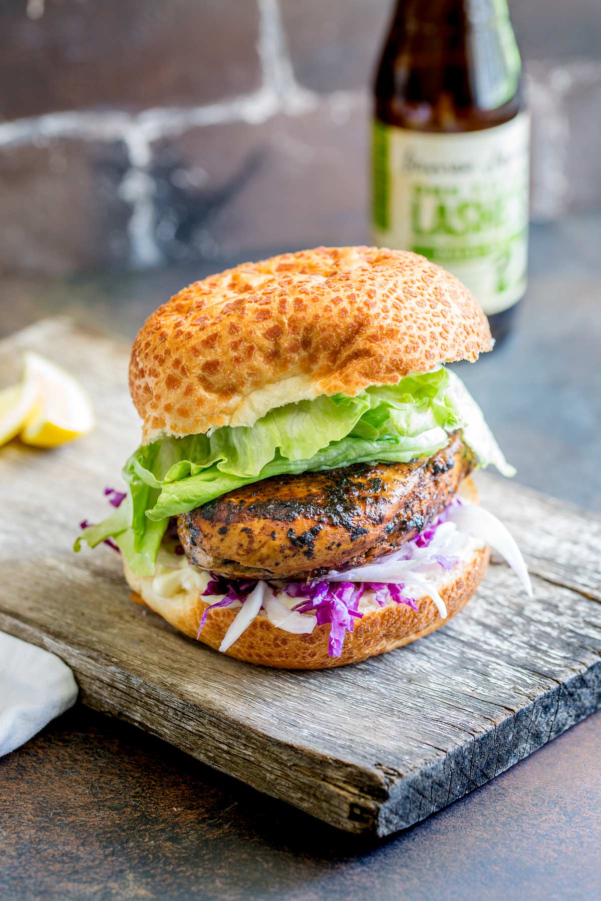 a burger on a wooden board on a dark table with dark brick in the background