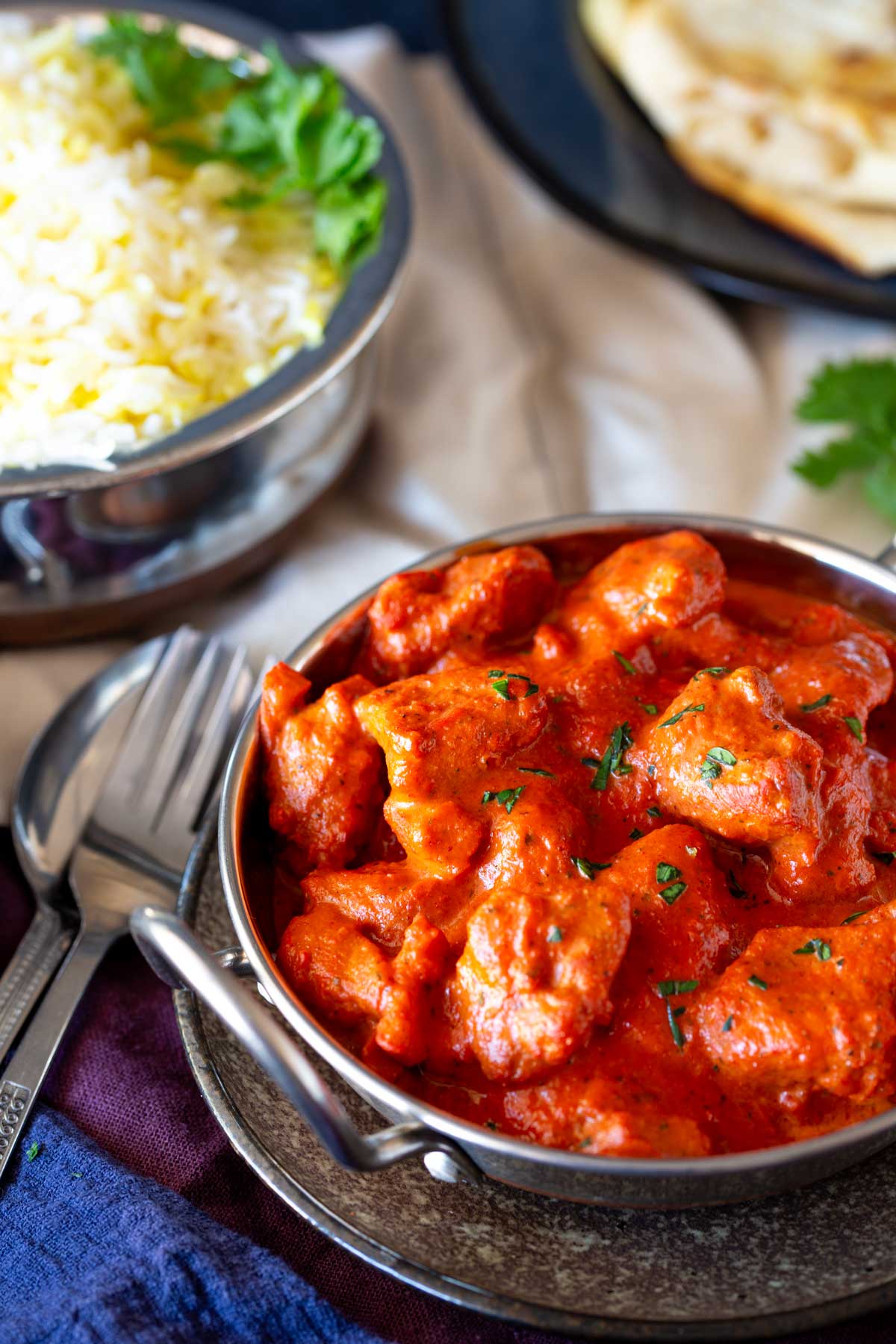 Creamy Chicken Chasni in a silver serving bowl on a bowl of rice behind it.