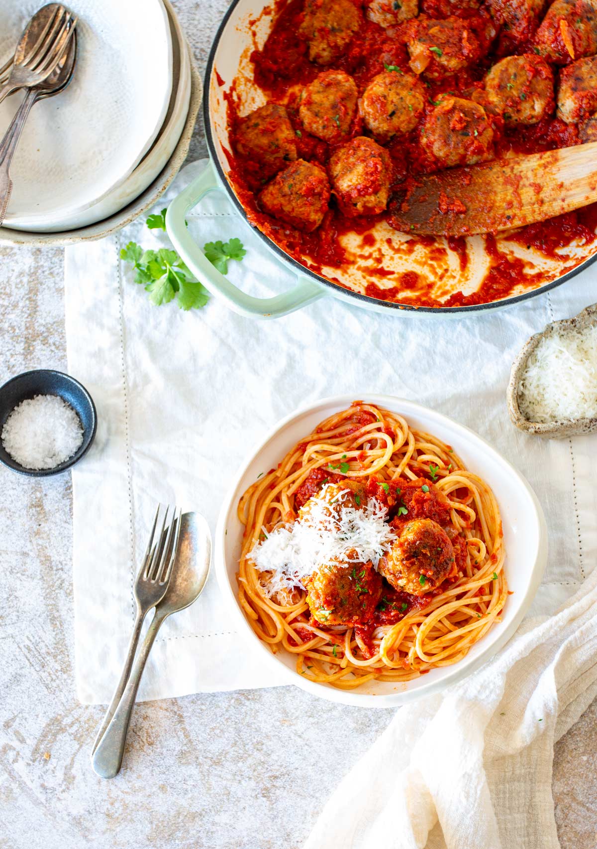 Rustic bowl of spaghetti and meatballs finished with grated Parmesan with pan of meatballs behind it