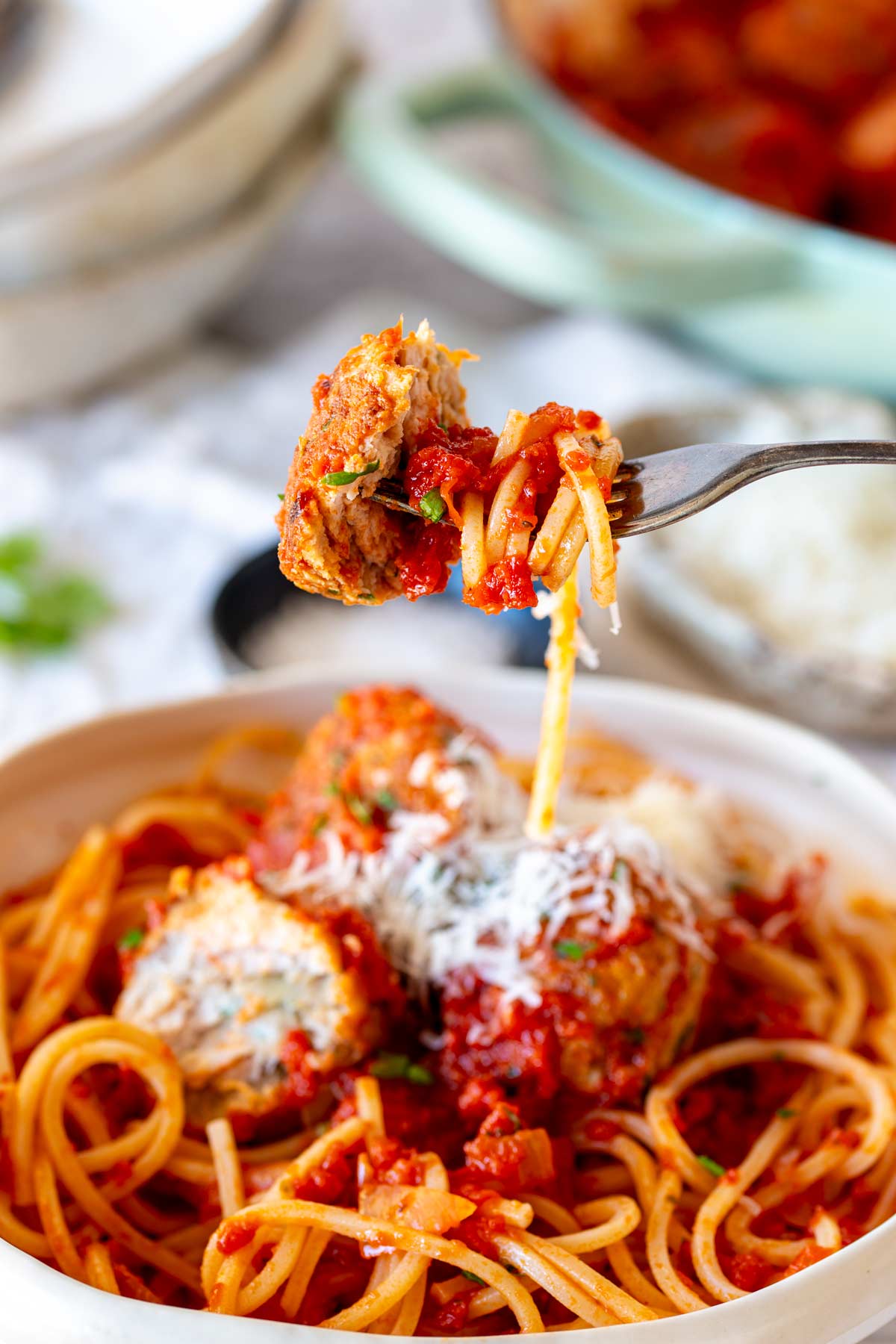 a fork lifting up some meatball and spaghetti from a white bowl