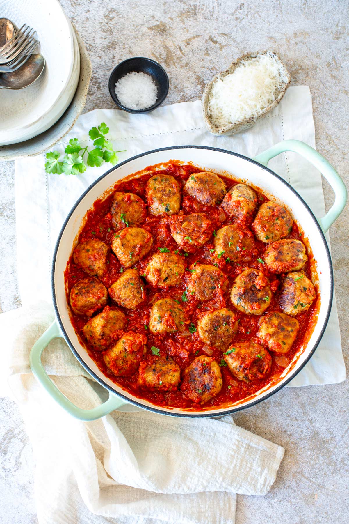 a skillet of meatballs in tomato sauce with cream napkin and pots of cheese and salt