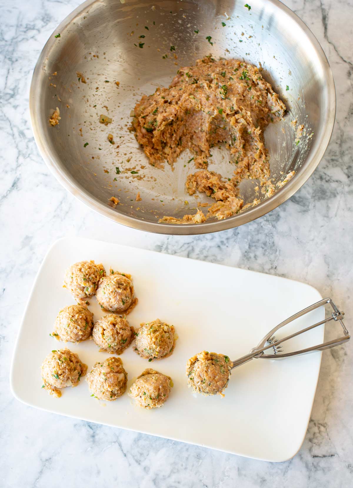a bowl of meatball mixture and a plate with a cookie scoop for making meatballs