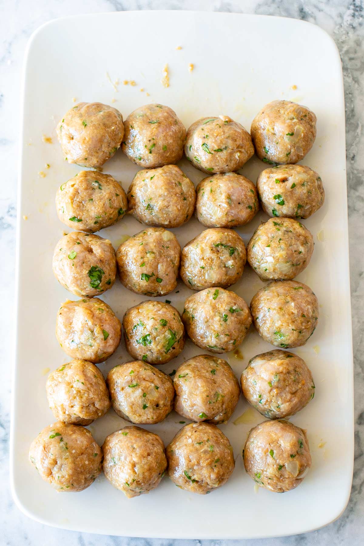 24 uncooked chicken meatballs on a white plate