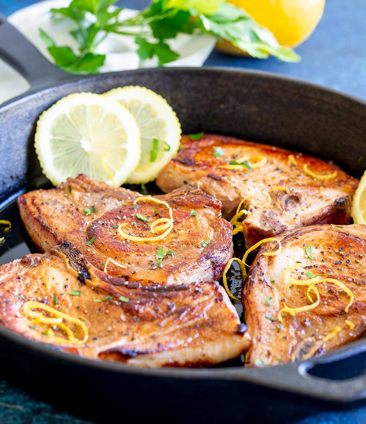 4 cooked chops in a pan with lemon and parsley in the background