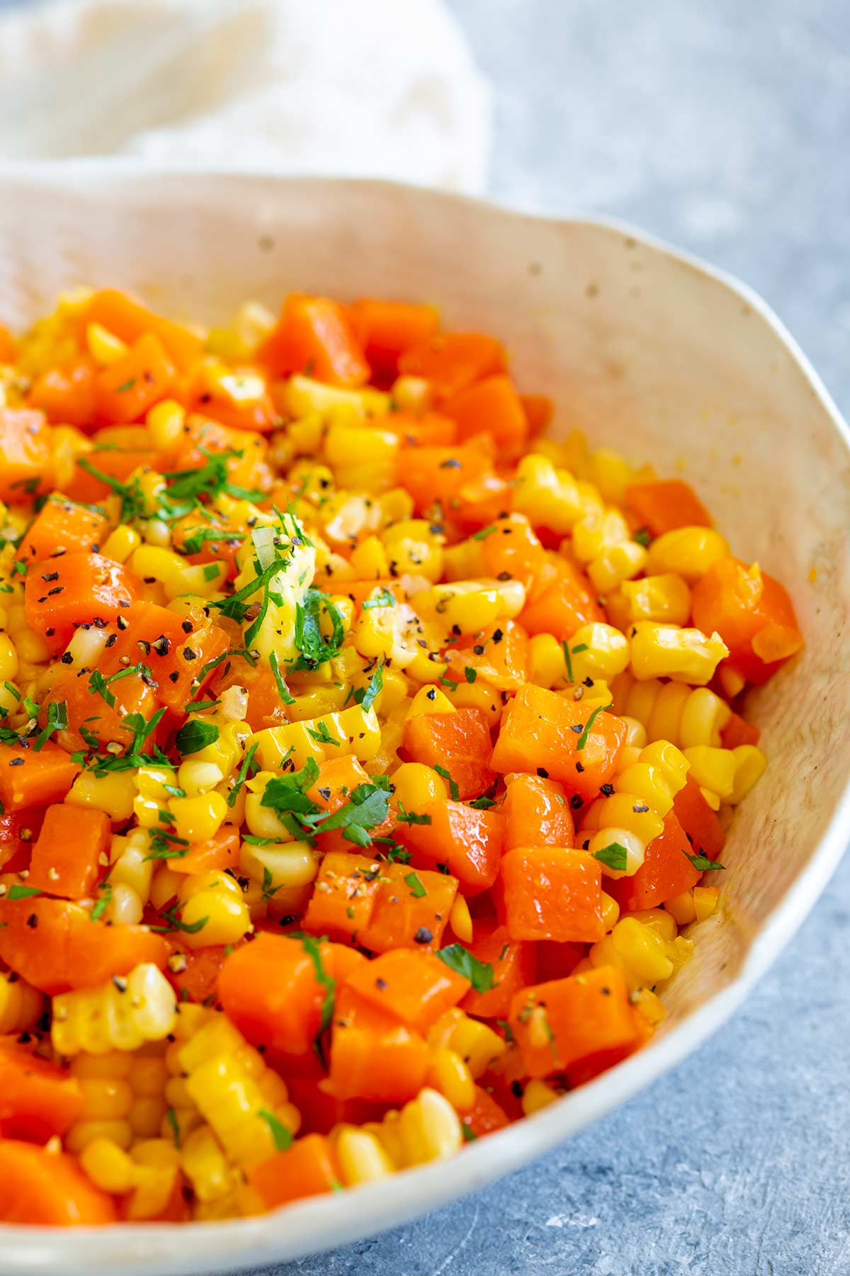 a whit bowl of chopped and buttered cooked carrots and corn