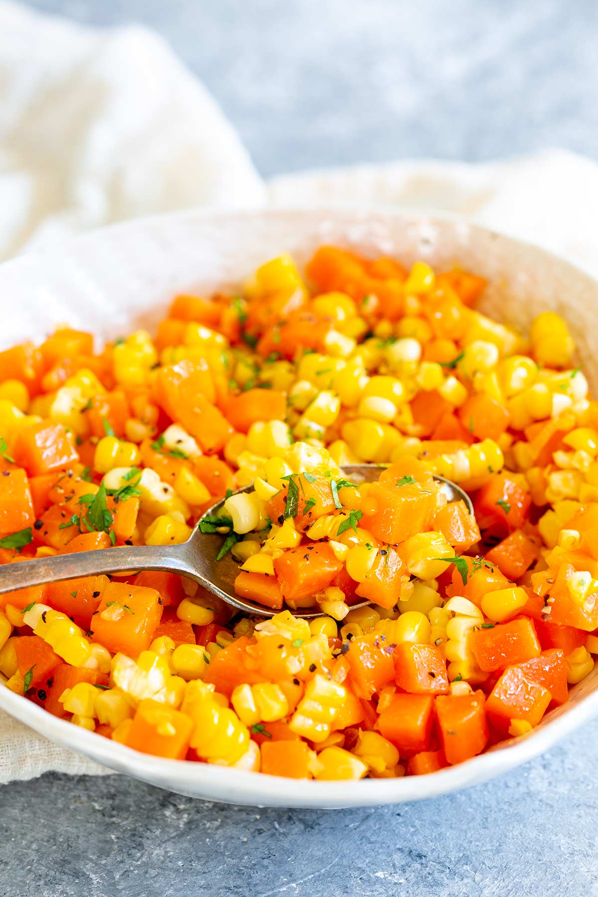 a spoon scooping up carrots and corn from a white bowl
