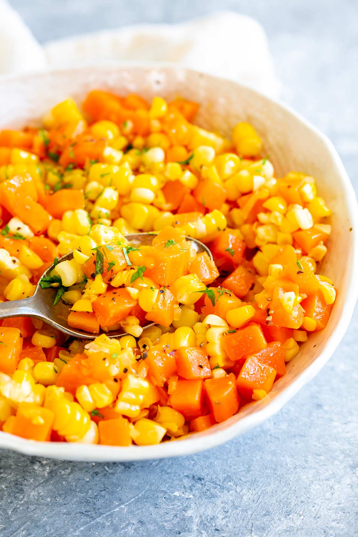 a whit bowl of carrots and corn on a grey table