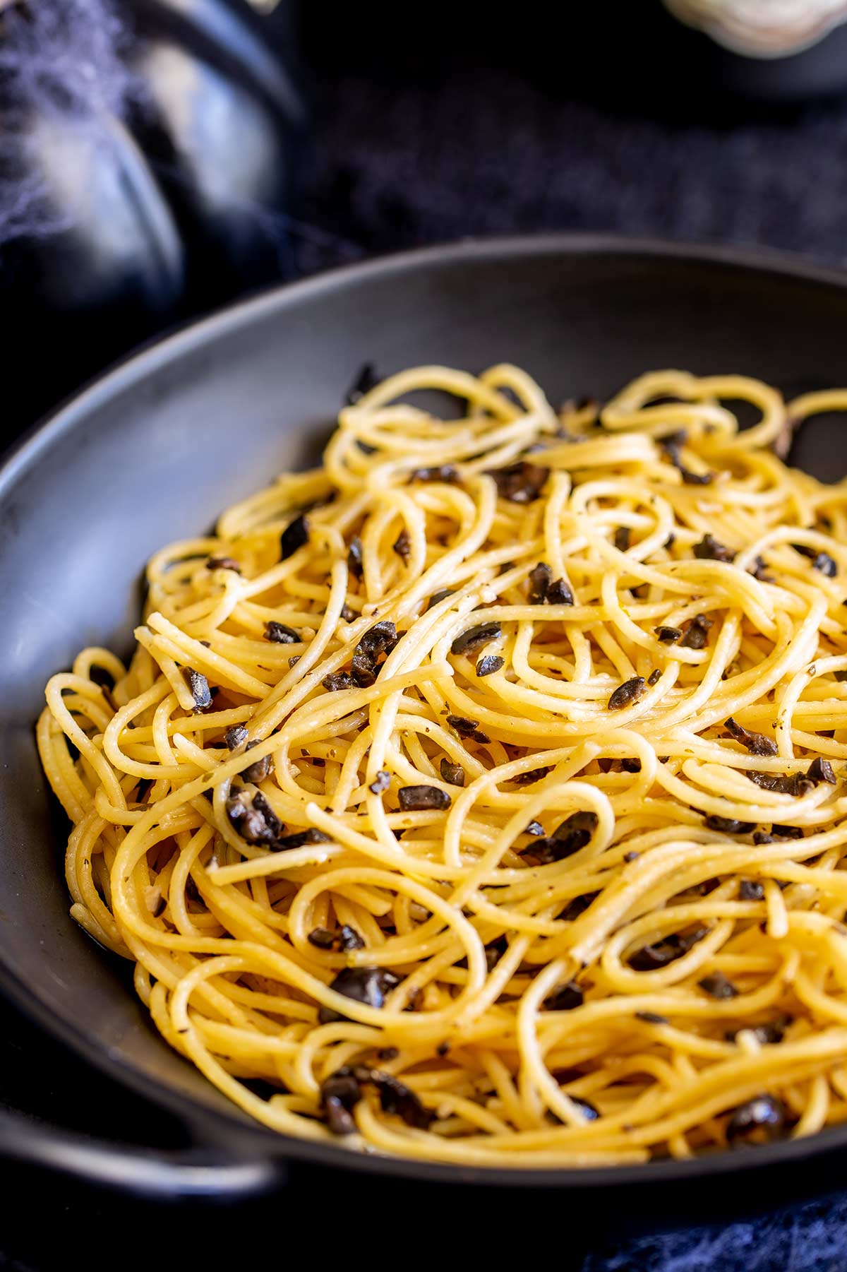 a black bowl filled with yellow pasta with black olive chunks