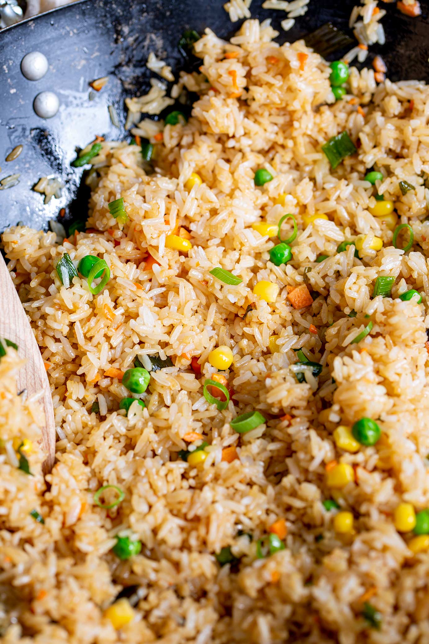 a wok of fried rice with peas, corn, carrots and green onion