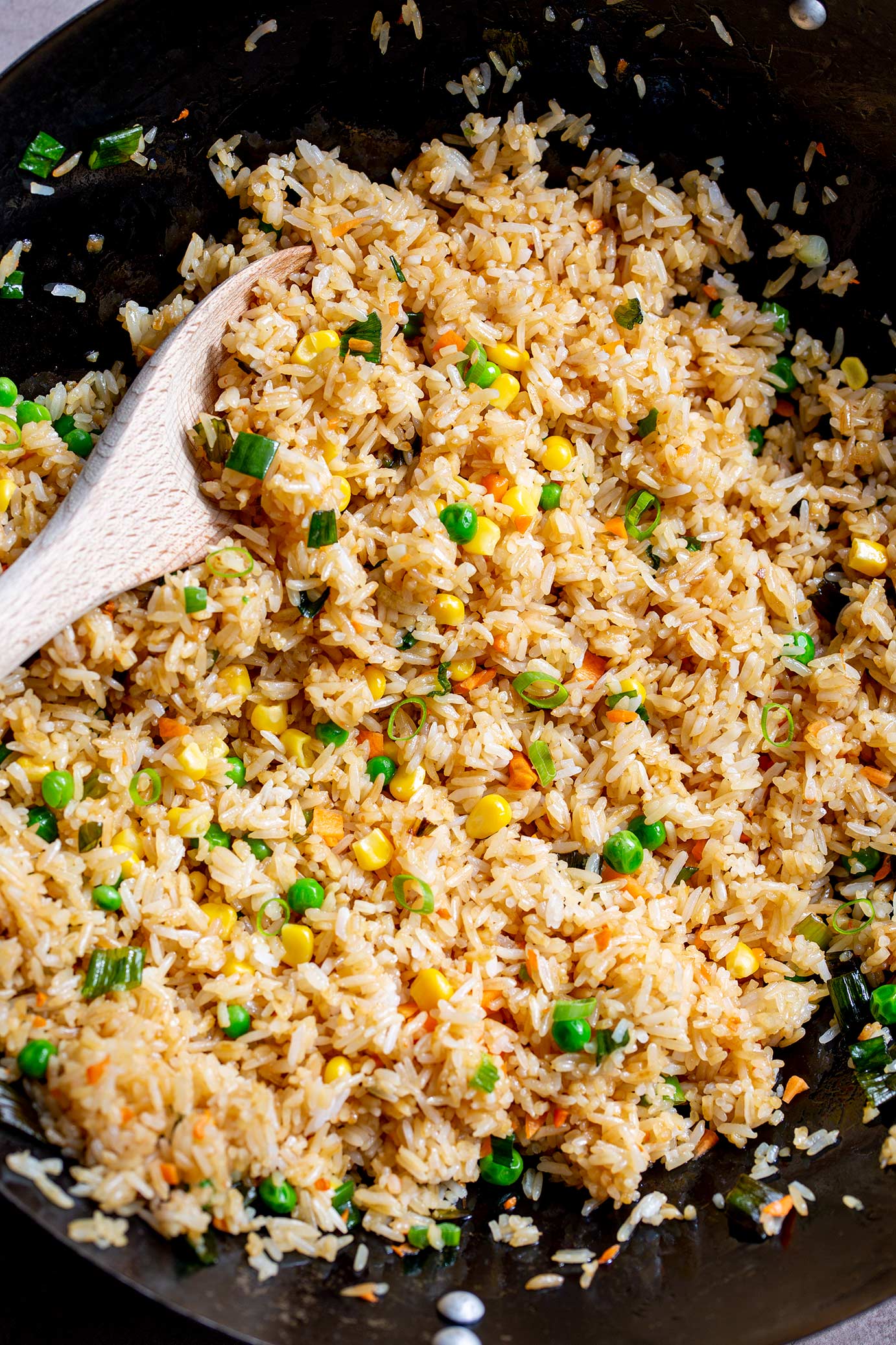 a wooden spoon in a wok full of fried rice