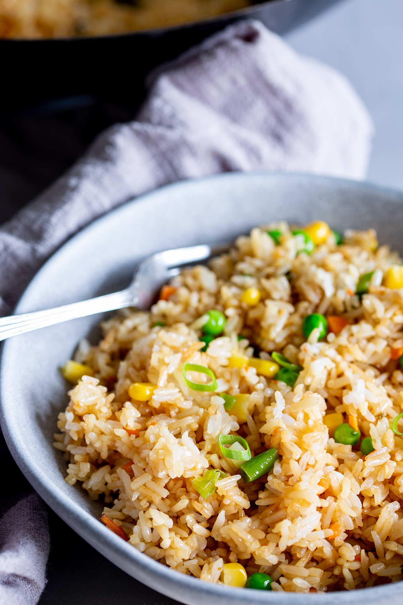 fried rice in a grey dish with a wok behind the bowl