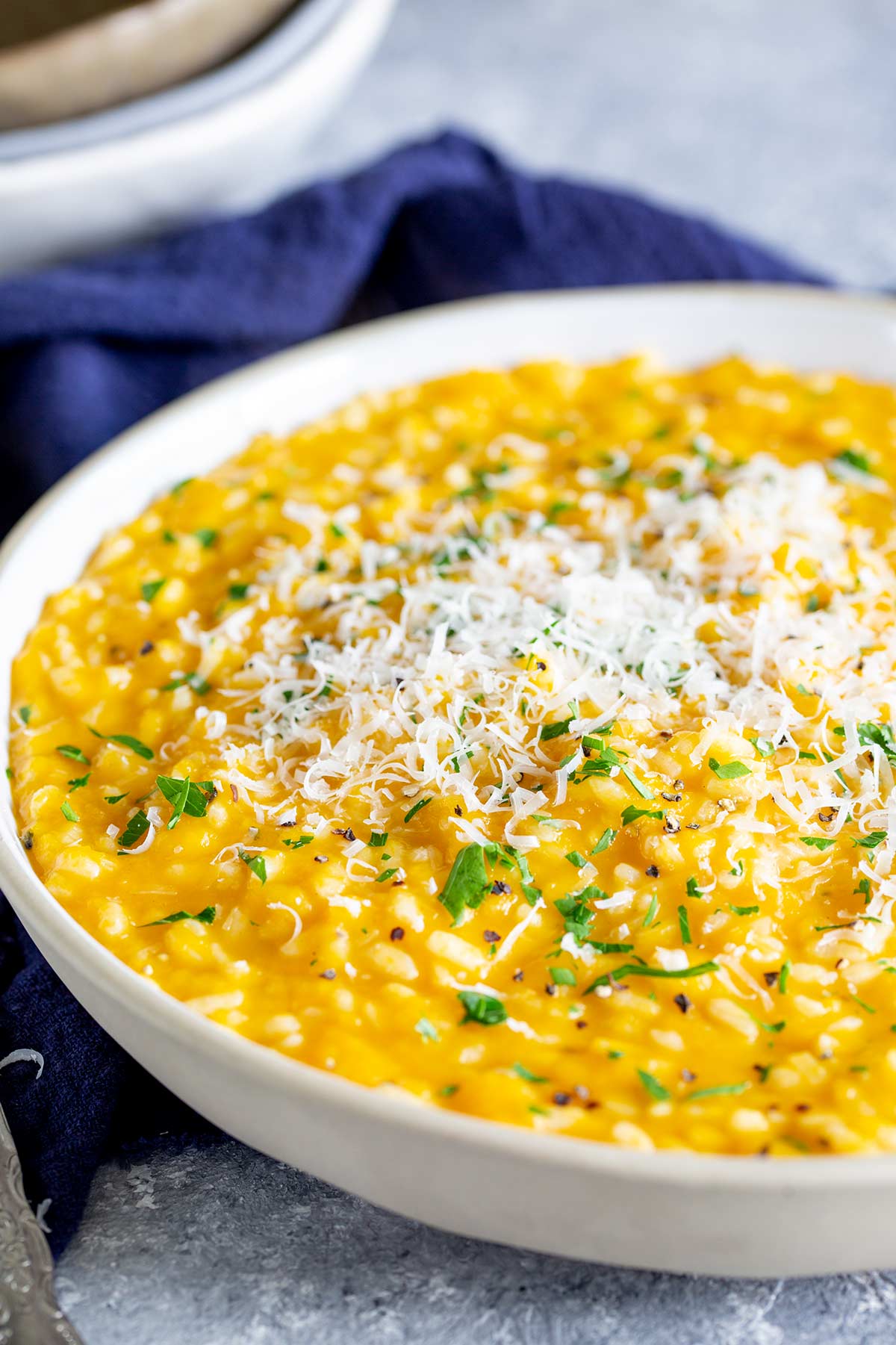 a large white bowl full of pumpkin risotto with parmesan on top