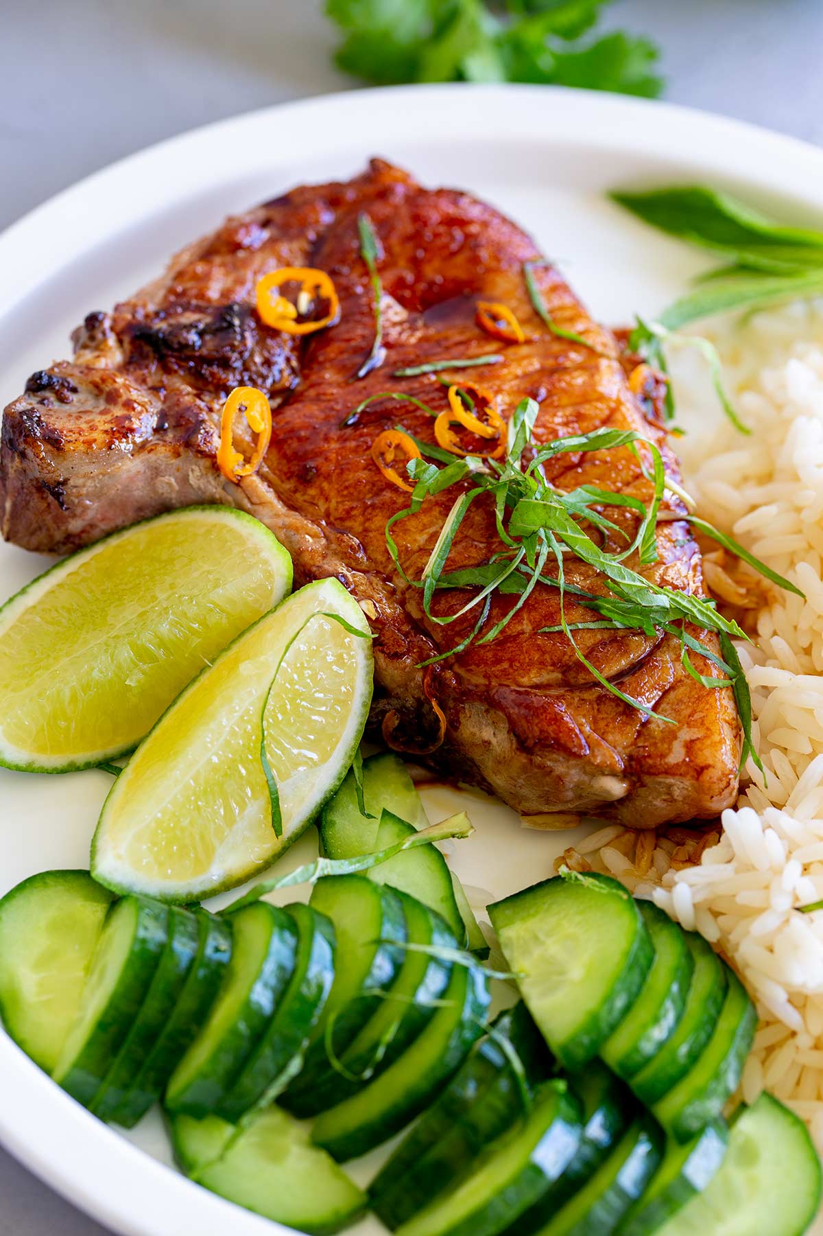 a cooked pork chop on a plate with rice, cucumber and lime